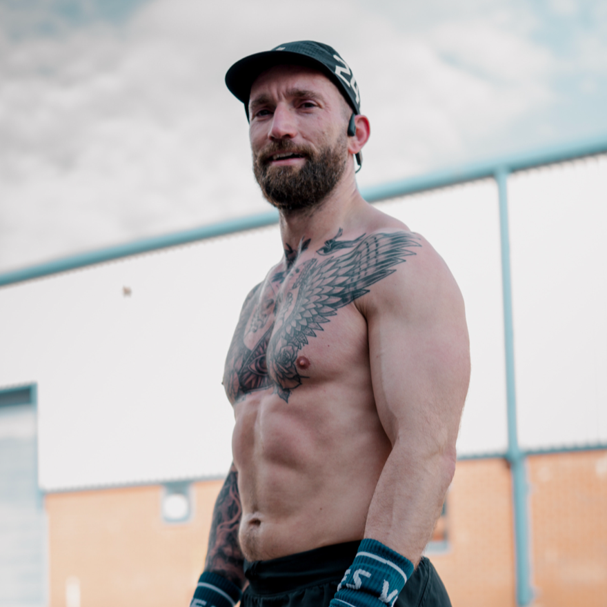 Man with tattoos outdoors wearing black shorts and a cap